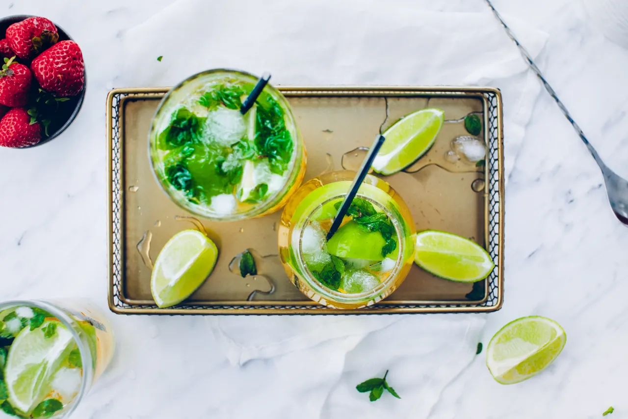 Orzeźwiający mohito drink co zamiast rumu? Lody, mięta i limonka w szklance. Obok miseczka truskawek.