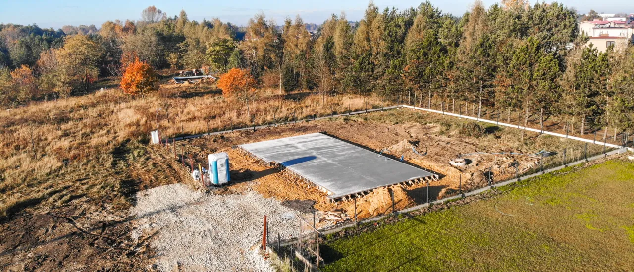 Plac budowy z betonową płytą fundamentową, gotową do dalszych prac. Wymiana gruntu pod płytę fundamentową zakończona.