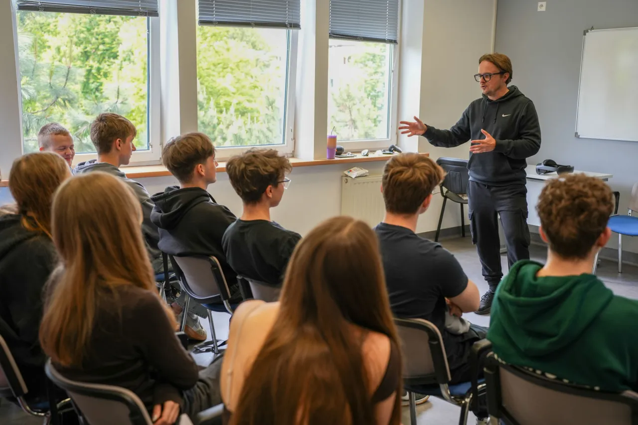 Prezentacja o tym, jak zostać nauczycielem bez studiów pedagogicznych. Mężczyzna w okularach przemawia do grupy uczniów.