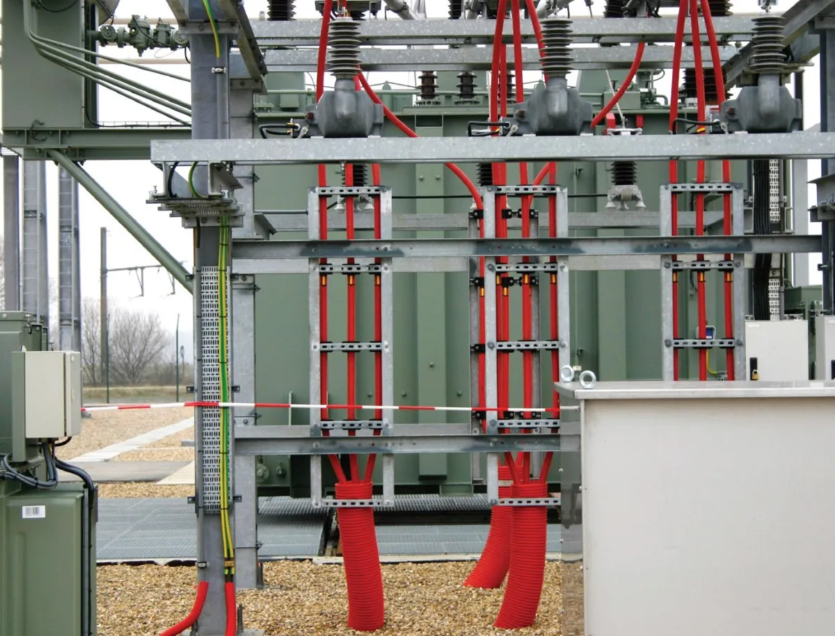Czerwone osłony kabli elektrycznych i skrętka obok transformatora na stacji energetycznej.