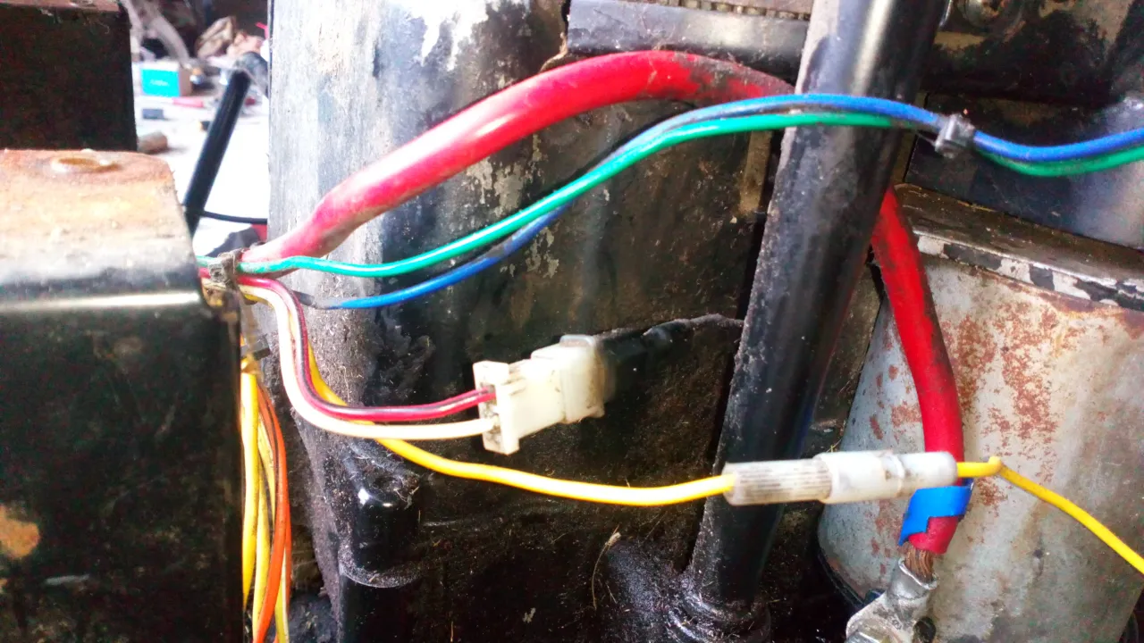 Instrukcja jak odpalić traktorek kosiarkę na krótko: połączenia kablowe, w tym czerwony, niebieski, zielony i żółty przewód, widoczne w pobliżu akumulatora.