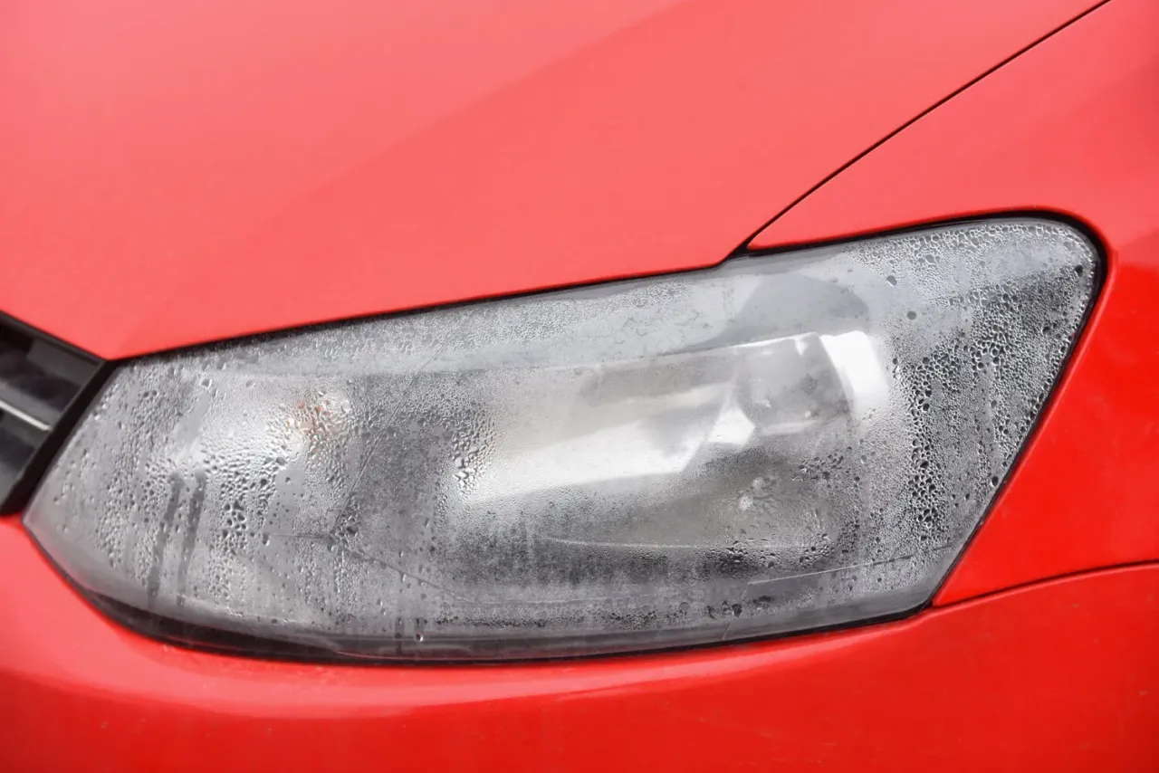 Parujące reflektory LED w nowym, czerwonym aucie, pokryte drobnymi kropelkami wilgoci.