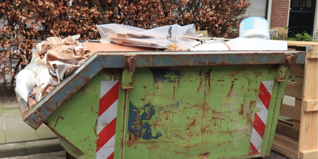 Zielony, zardzewiały kontener na śmieci wypełniony odpadami. Zastanawiasz się, ile kosztuje kontener na śmieci Warszawa?