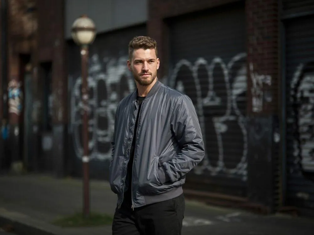 mężczyzna w stylowej kurtce bomberce na tle miasta