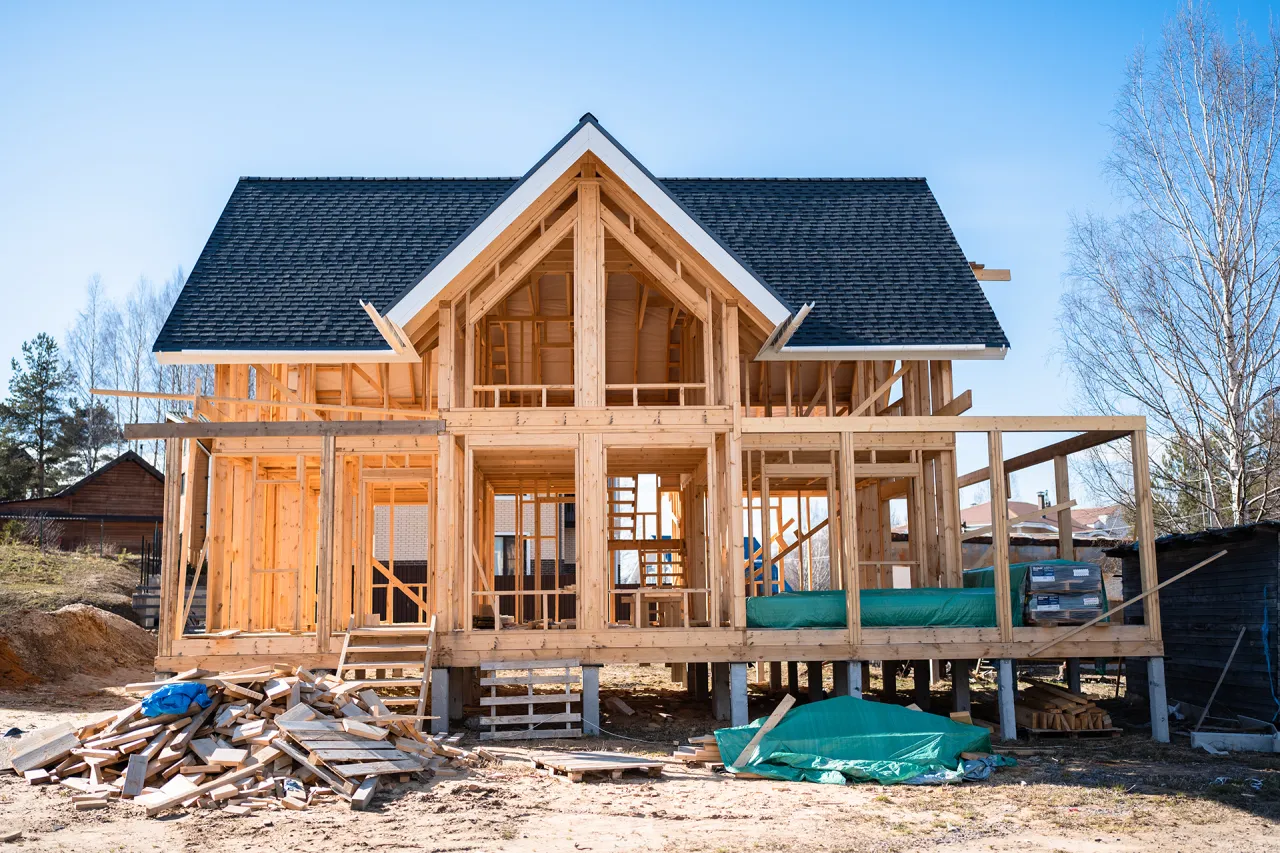 Budowa domu drewnianego pod klucz w toku. Widoczna konstrukcja szkieletowa, dach, materiały budowlane.