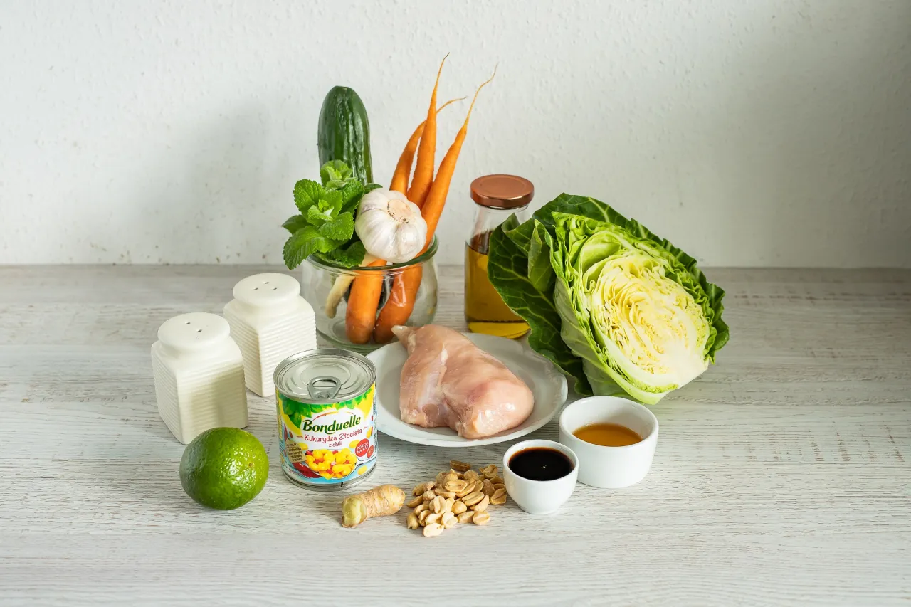 Składniki na sałatkę tajską z kurczakiem: pierś kurczaka, kapusta, marchew, og&oacute;rek, czosnek, imbir, limonka, orzeszki ziemne, kukurydza, sos sojowy i olej.