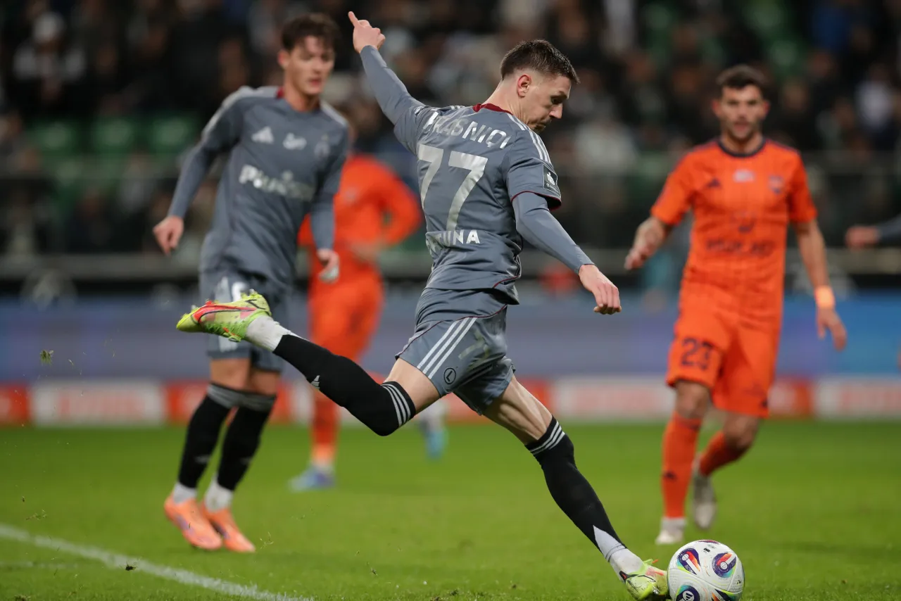 Piłkarz w szarym stroju z numerem 77, Matty Cash, wykonuje strzał. Jego wzrost pozwala mu na mocne uderzenie.