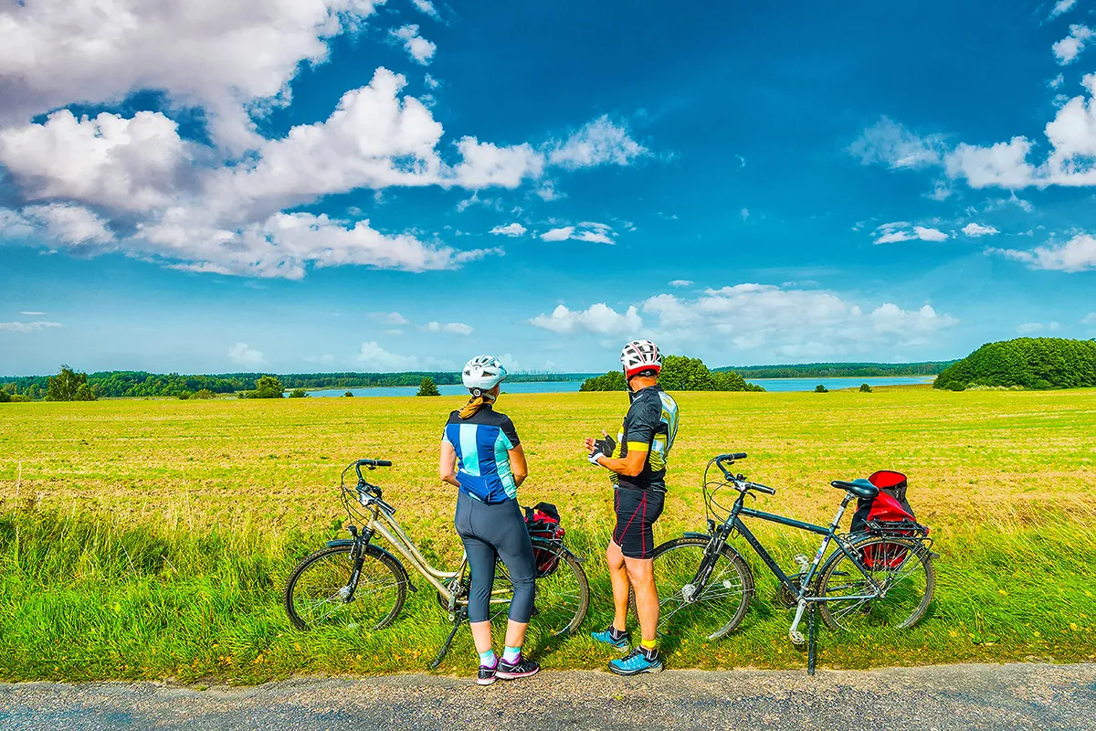 Para rowerzyst&oacute;w na malowniczej trasie koło Szczytna, odpoczywających na tle jeziora i p&oacute;l.