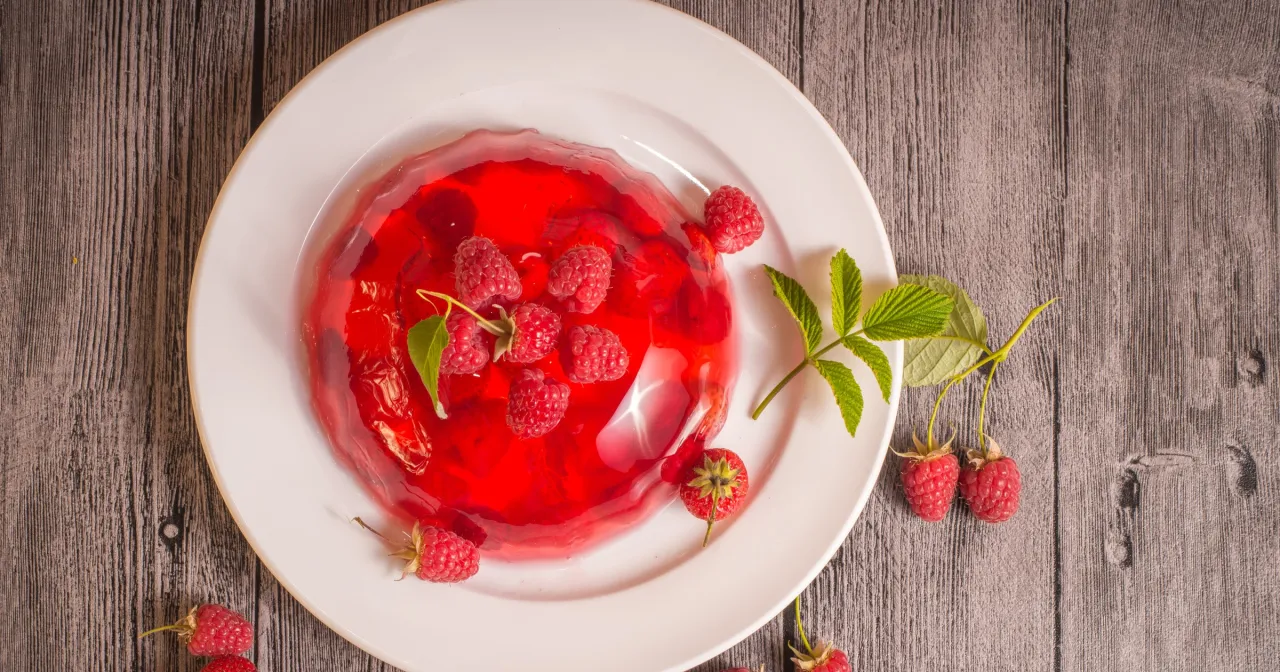 Czerwona galaretka owocowa z malinami na białym talerzu. Czy galaretka owocowa jest zdrowa? Zależy od składników.
