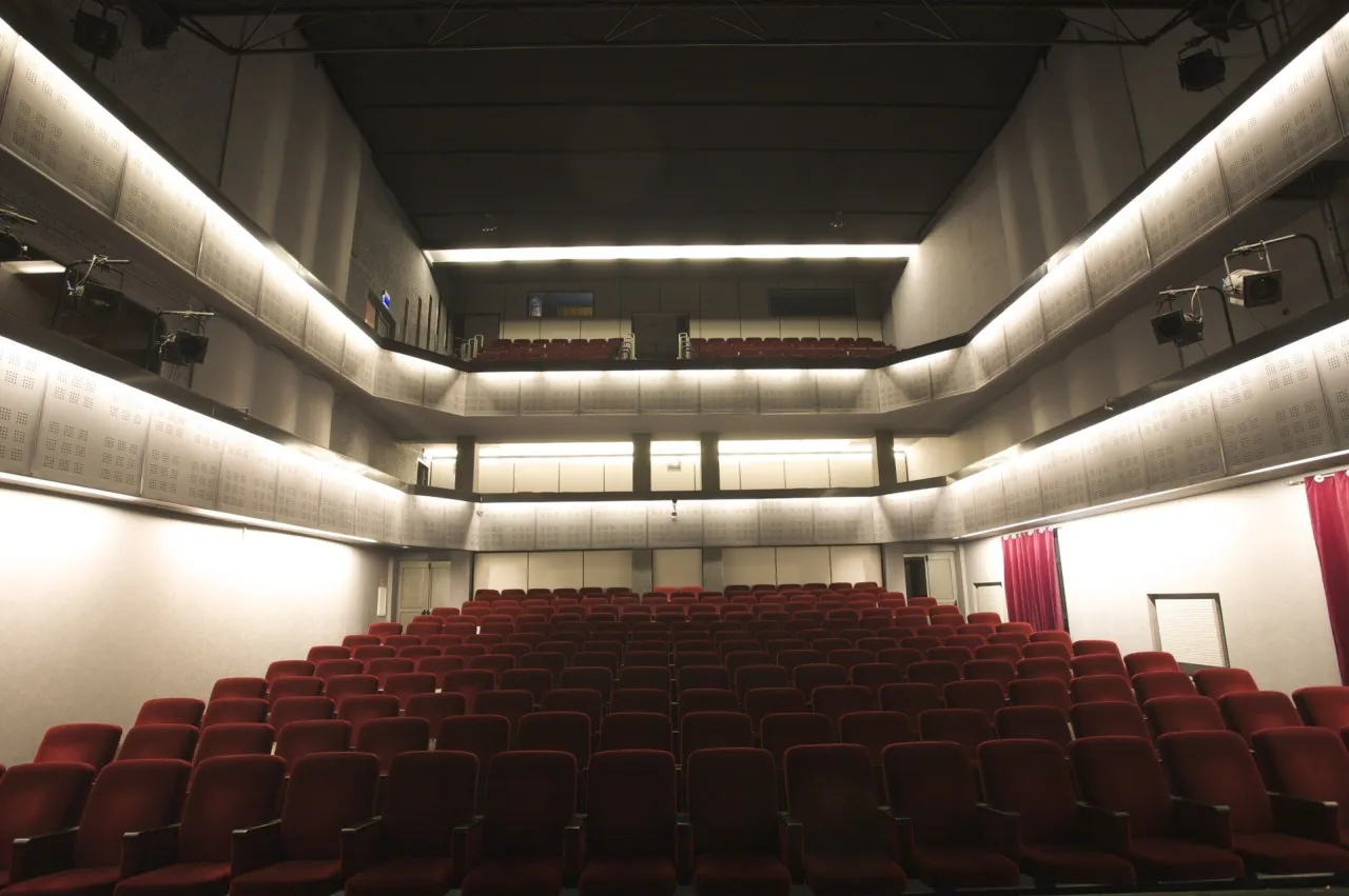 Widok na puste rzędy czerwonych foteli w teatrze Bagatela. Widać piętrową widownię, z lożą lub balkonem na g&oacute;rze.