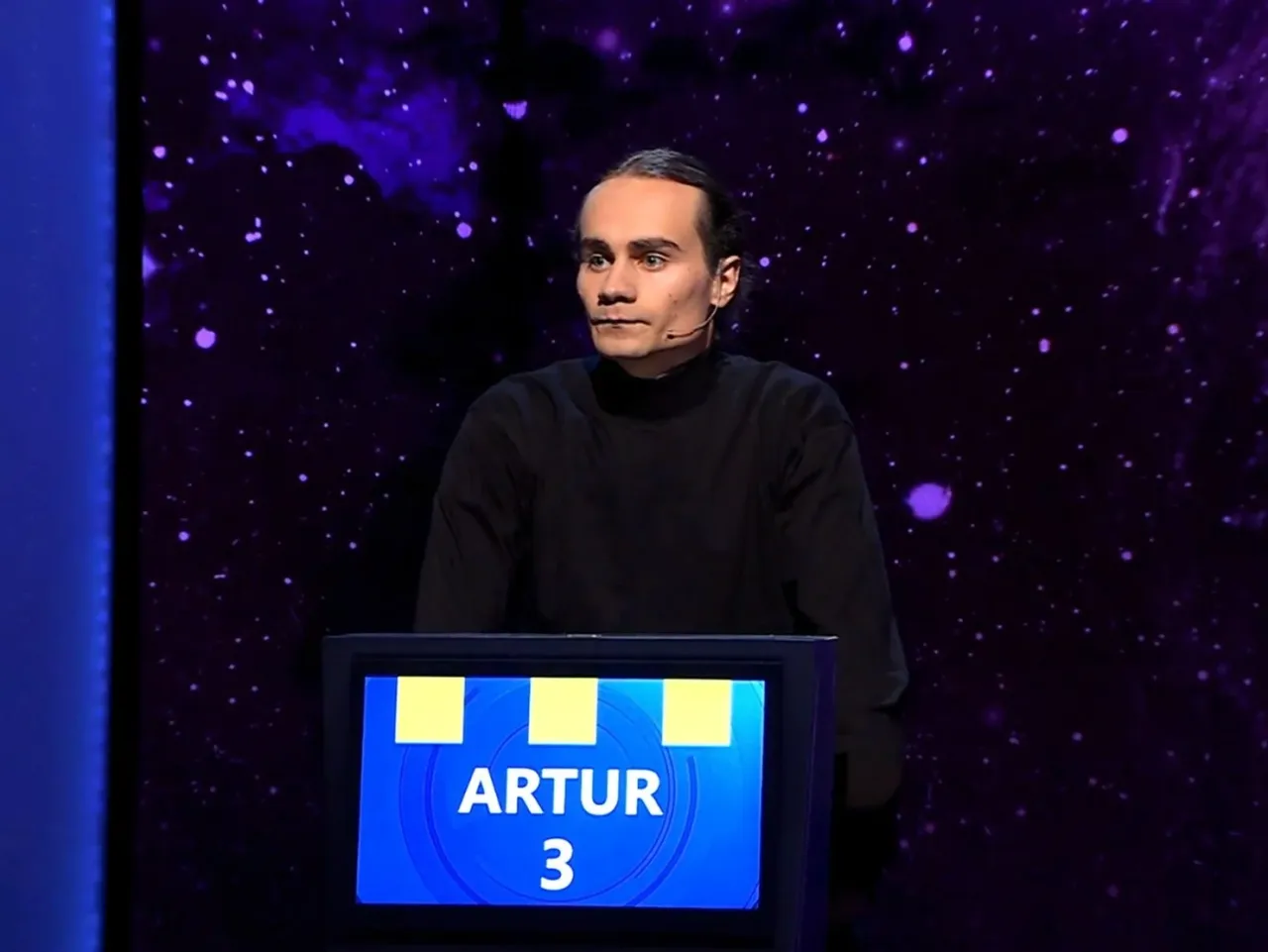 Artur, jeden z dziesięciu wielki finał kiedy, stoi przed niebieskim panelem z jego imieniem i numerem 3.