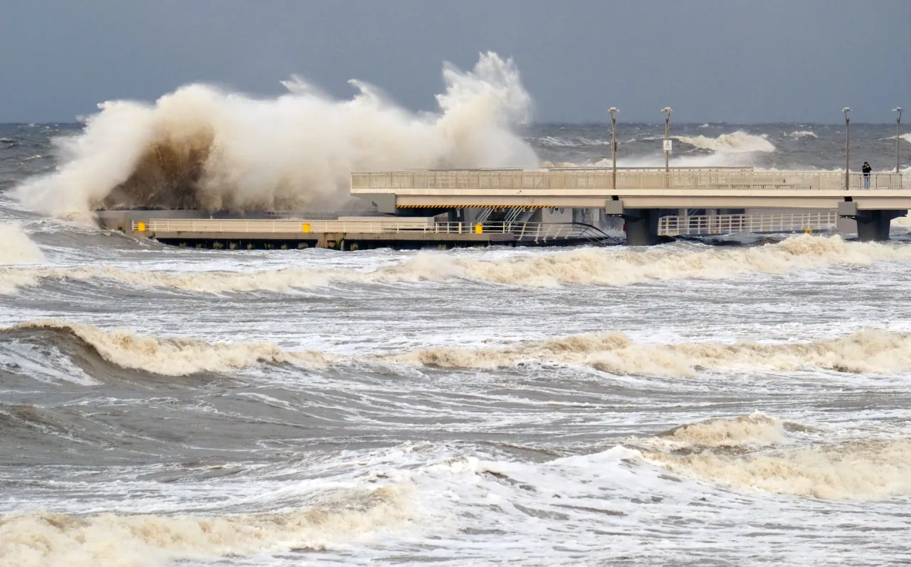 Potężne fale rozbijają się o molo, kiedy sztorm na Bałtyku pokazuje swoją siłę. Woda jest wzburzona, a niebo ciemne.