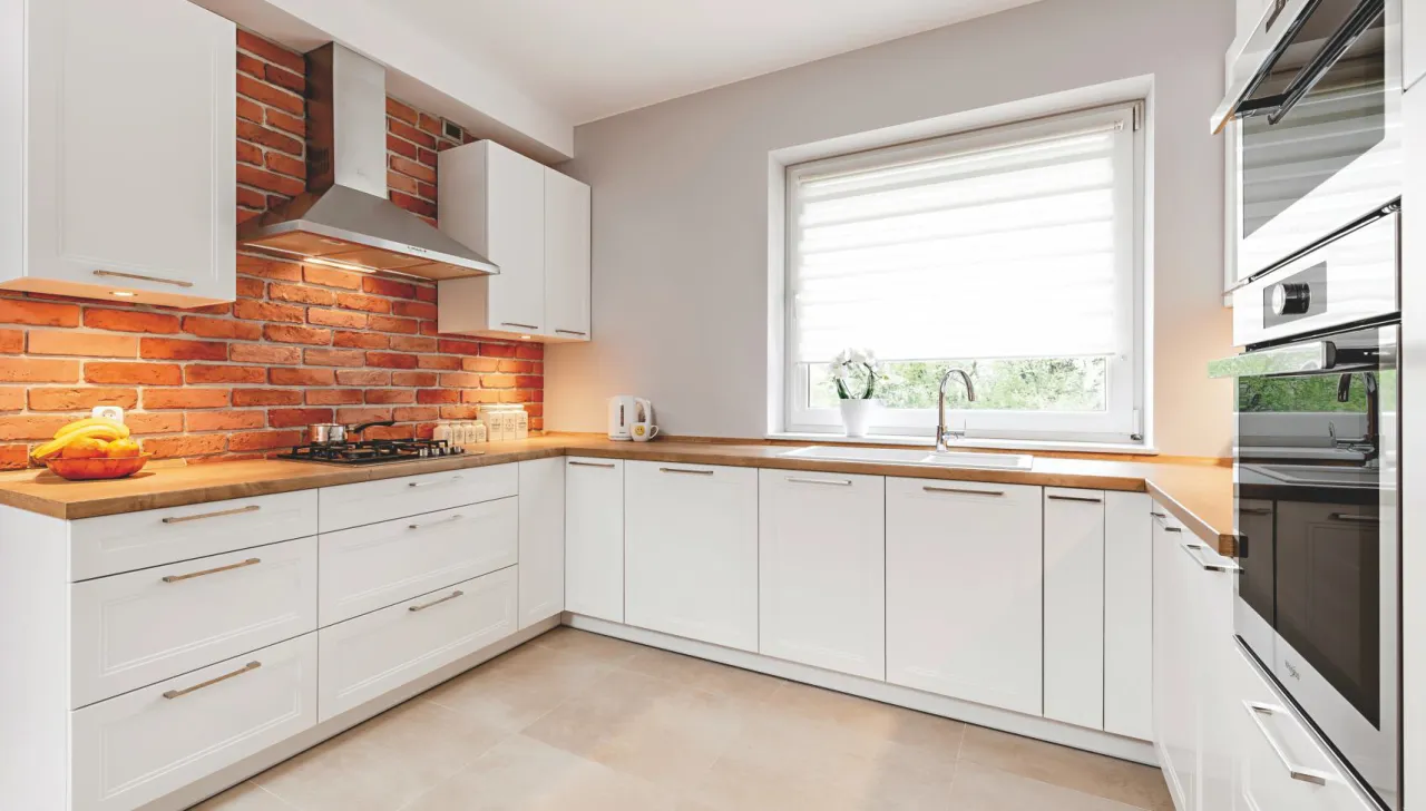 kuchnia z białymi meblami drewnianym blatem i ścianą z cegły