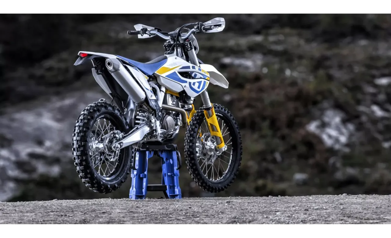 Husqvarna 250 FE gotowy na teren. Biało-niebieski motocykl z żółtymi akcentami na amortyzatorach.