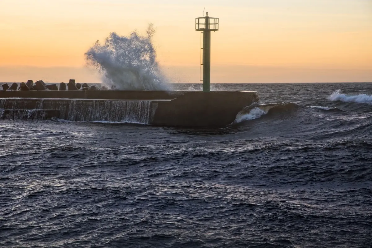 Fala rozbija się o falochron z latarnią, zapowiadając sztorm na Bałtyku.