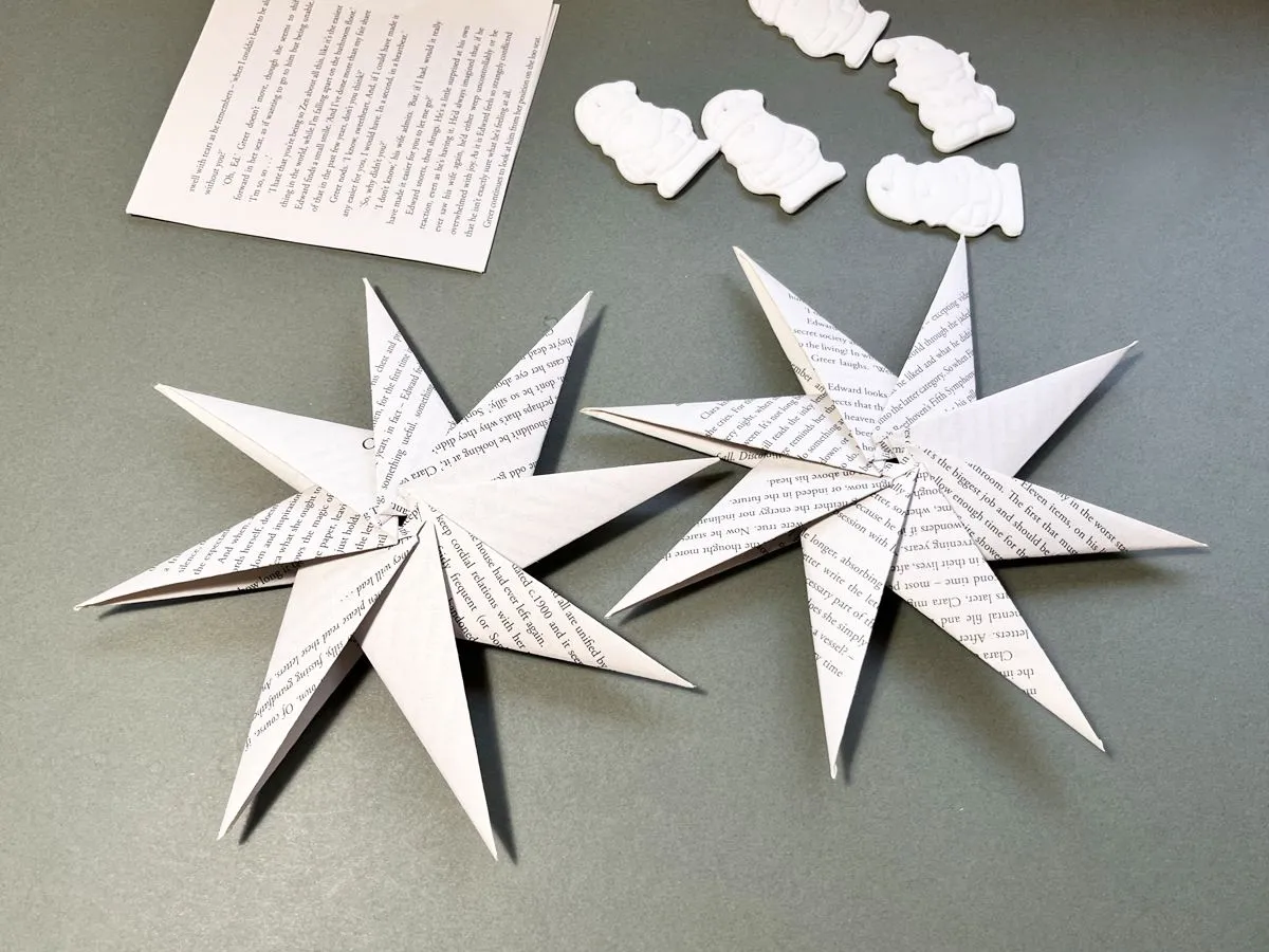 Jak zrobić gwiazdę na choinkę? Dwie papierowe gwiazdy z książki, obok ozdoby z masy solnej.