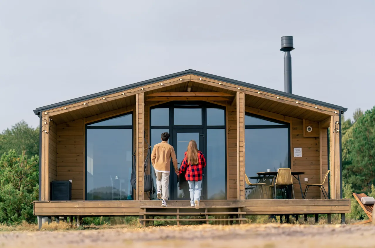 Para, trzymając się za ręce, wchodzi do nowoczesnego domku. To idealne miejsce na inwestycję, zapewniające wysoką rentowność wynajmu domk&oacute;w letniskowych.