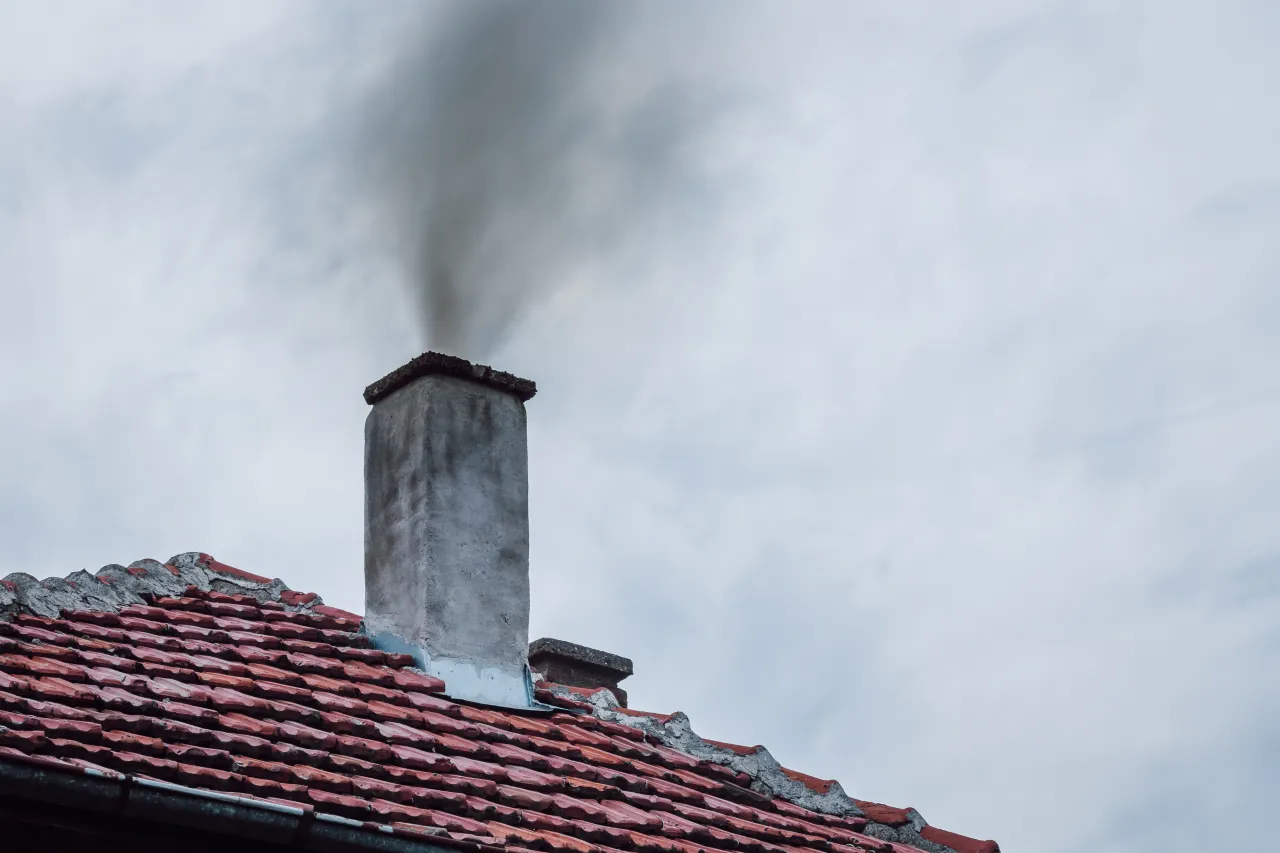 Dym wydobywa się z komina na dachu pokrytym czerwona dach&oacute;wką. Zastanawiasz się, ile kosztuje czyszczenie komina?