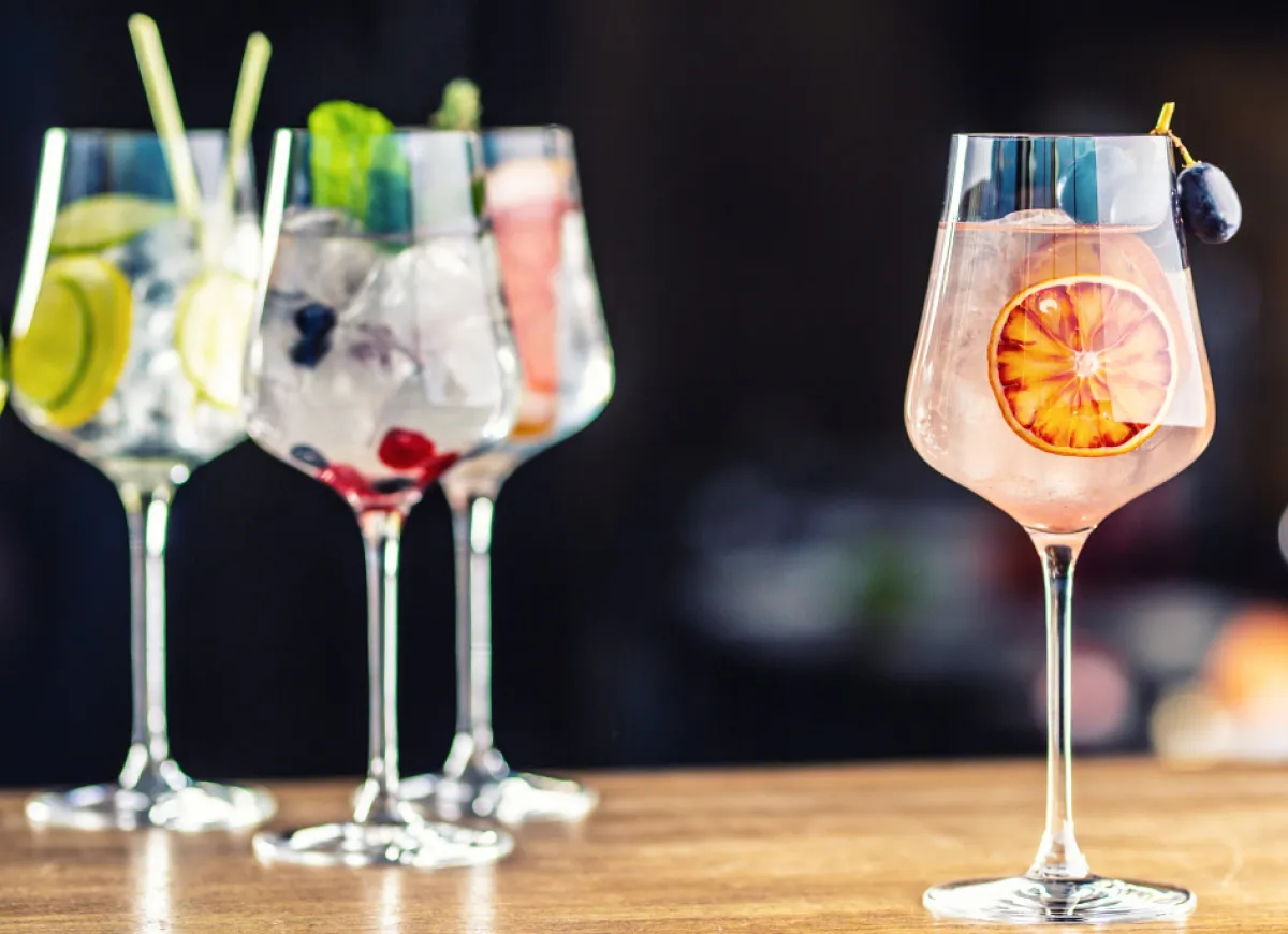 Orzeźwiający drink z wódką i owocami leśnymi, obok drink z ginem z plasterkiem pomarańczy i winogronem.