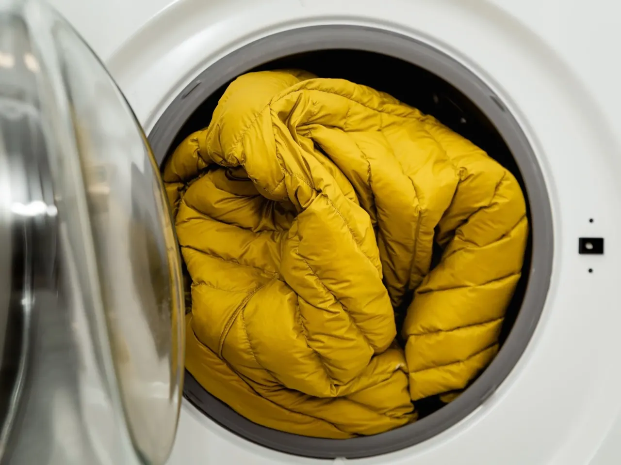 Ż&oacute;łta kurtka puchowa w pralce. Użyj specjalnych piłeczek do prania kurtek puchowych, by zachować jej objętość.