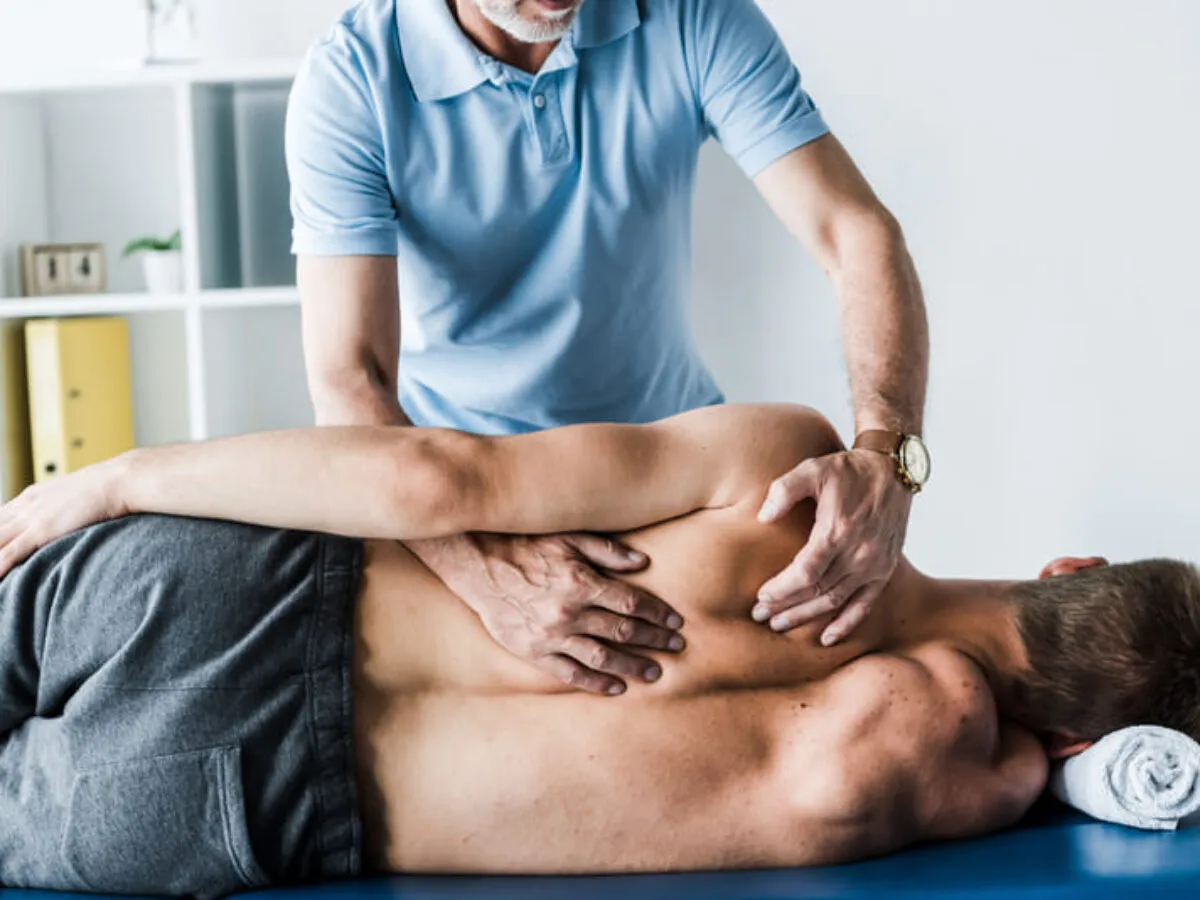 Fizjoterapeuta wykonuje masaż plec&oacute;w, pomagając w rehabilitacji po złamaniu kręgosłupa lędźwiowego.