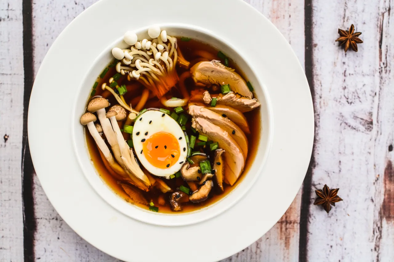 Aromaticzny ramen z kaczki z jajkiem na p&oacute;ł, grzybami enoki i shiitake, posypany szczypiorkiem.