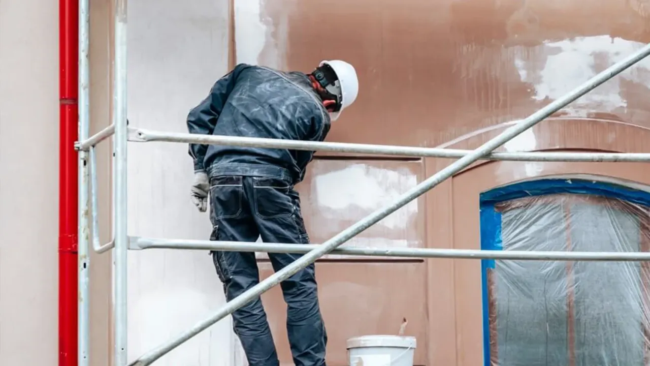 Robotnik na rusztowaniu maluje elewację. To właśnie co to znaczy modernizacja – odnawianie i ulepszanie budynków.