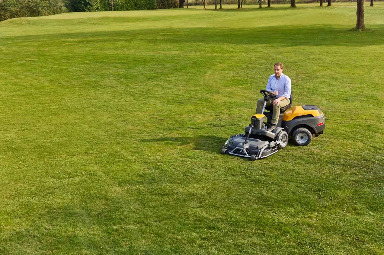 Mężczyzna siedzi na traktorku ogrodowym, gotowy do koszenia. Pokazano, jak ustawić kosisko w traktorku, aby uzyskać idealnie przystrzyżony trawnik.