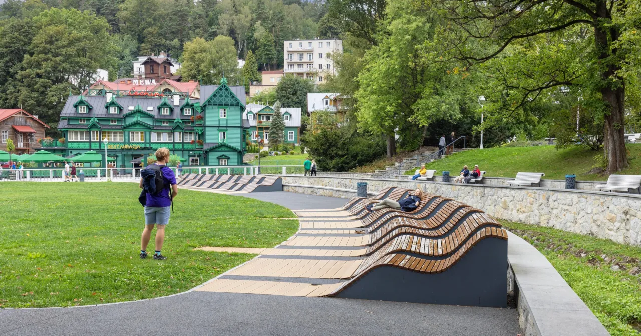 Zielony budynek sanatorium w Krynicy-Zdroju, z widokiem na park i turystów. Sprawdź sanatorium Krynica Zdrój cennik.