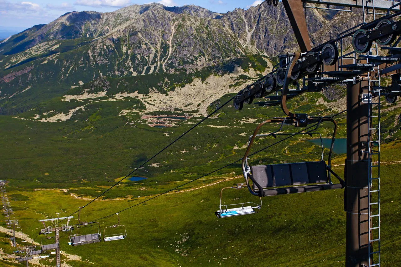 Kolejka linowa na Kasprowy Wierch w Tatrach. Krzesełka wspinają się pośr&oacute;d zielonych zboczy i skalistych szczyt&oacute;w.