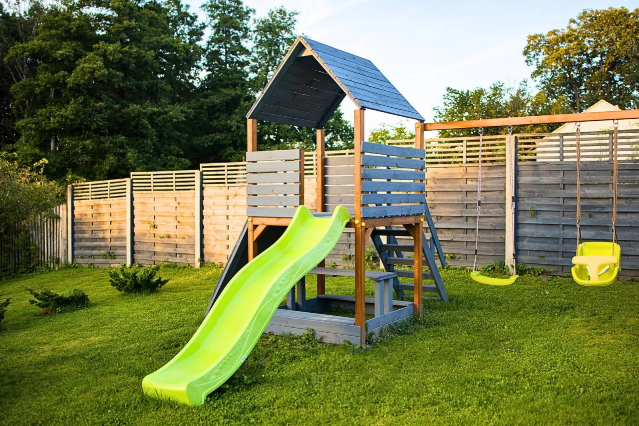 Nowy domek dla dzieci projekt: zjeżdżalnia, piaskownica i huśtawki na zielonym trawniku.
