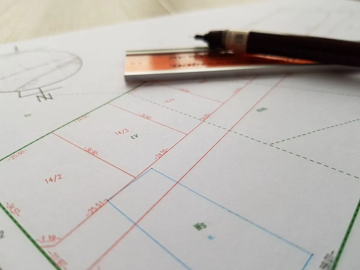 Mapa geodezyjna z zaznaczonymi działkami i wymiarami, przybory kreślarskie. Dokumentacja do sądowy podział nieruchomości procedura.