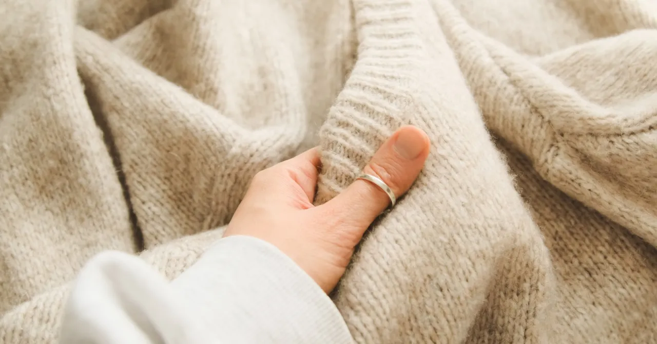 Delikatna dłoń z pierścionkiem dotyka beżowego, sfilcowanego swetra. Co zrobić, by go uratować?