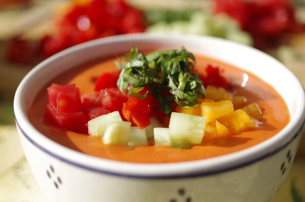 Chłodnik z pomidorów, ozdobiony kostkami pomidora, ogórka i papryki, z listkami bazylii na wierzchu. Idealny na upalne dni.