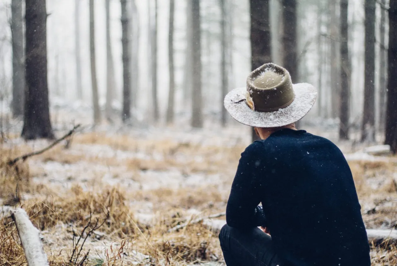 Mężczyzna w kapeluszu siedzi w zimowym lesie, wsłuchując się w ciszę. To idealny moment, by zastanowić się, jak rozwijać intuicję.