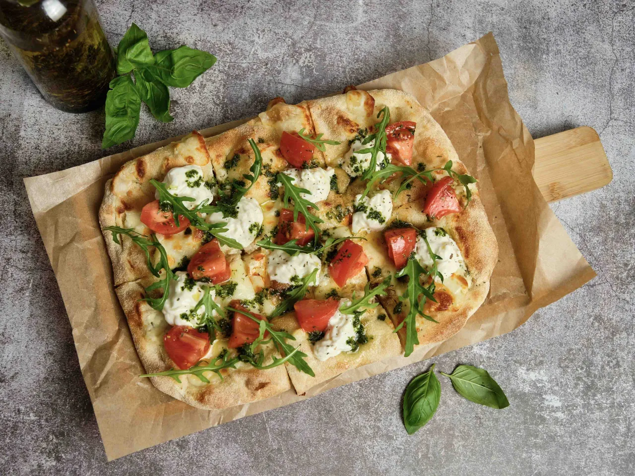 Pizza wegetariańska z pomidorami, mozzarellą i rukolą, polana zielonym sosem. Idealna na lekki posiłek.