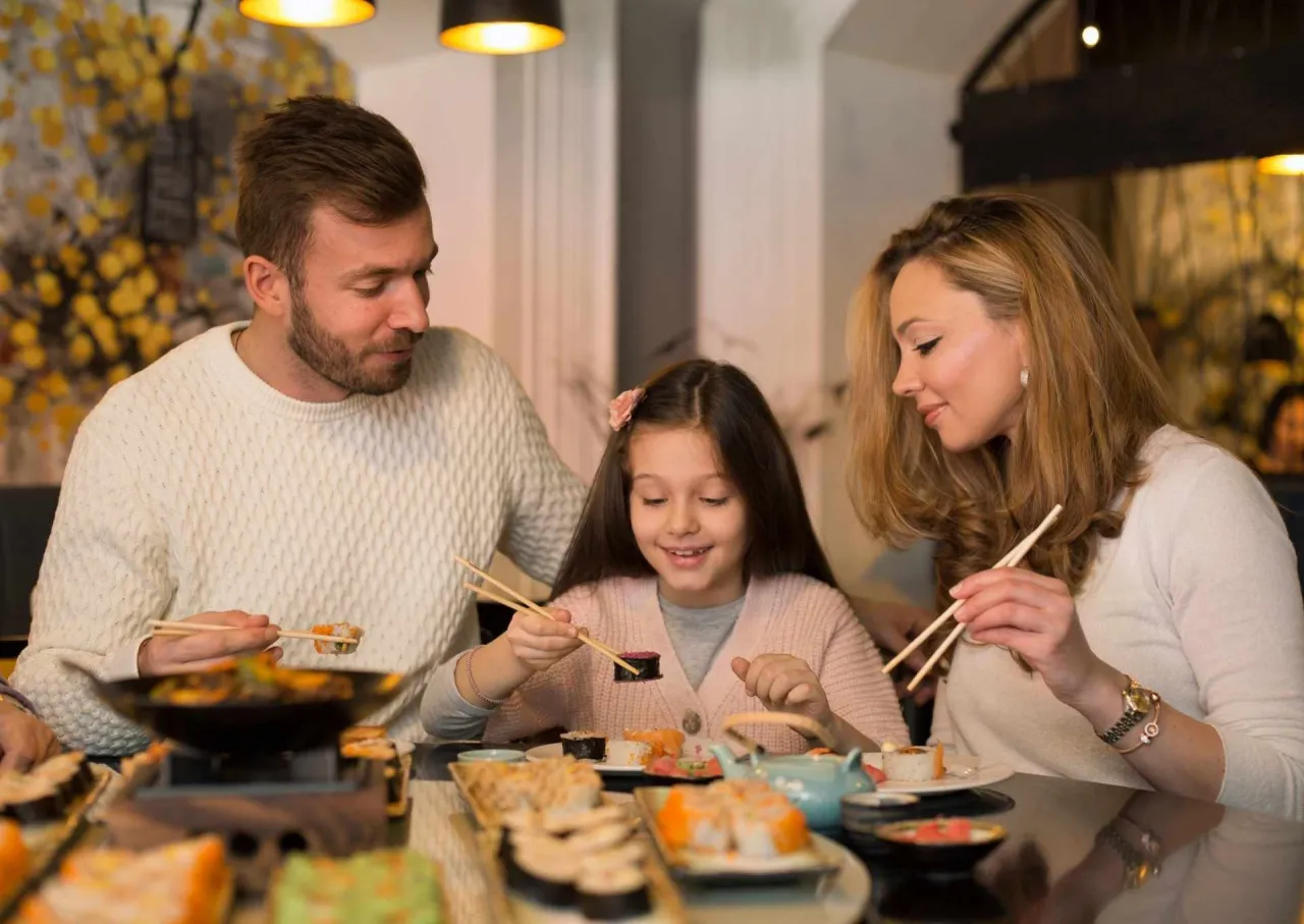 Rodzina przy stole, gdzie ojciec, matka i córka jedzą sushi. Czy dzieci mogą jeść sushi? Ta uśmiechnięta dziewczynka z pewnością tak!
