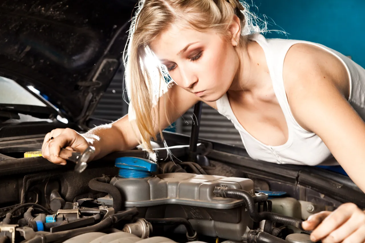 Kobieta z kluczem przy silniku. Zastanawia się, co ile wymiana oleju w nowym samochodzie jest konieczna.