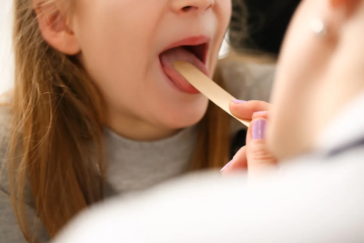 Lekarz bada gardło dziecka, szukając odpowiedzi na pytanie, co na b&oacute;l gardła u dziecka.