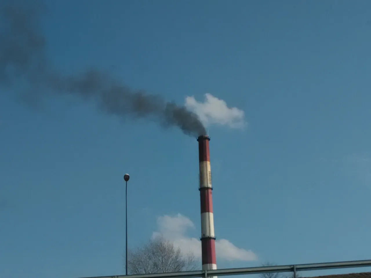 Czarny dym z komina oznacza zanieczyszczenie powietrza. Widać go na tle błękitnego nieba.