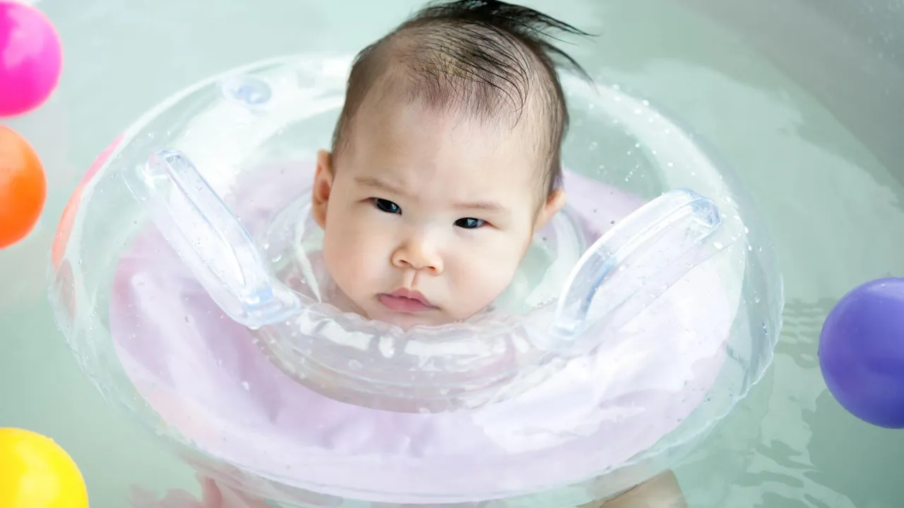 Urocze niemowlę w k&oacute;łku do pływania dla rocznego dziecka, otoczone kolorowymi piłeczkami.