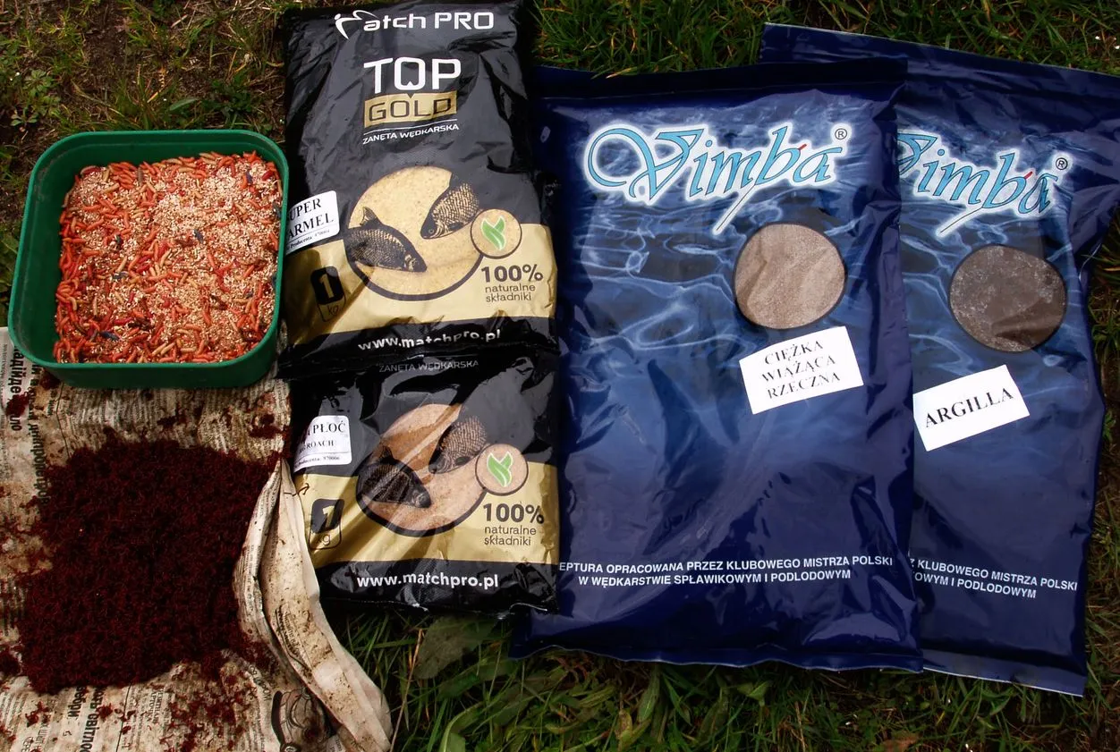 Zestaw zanęt Match Pro: Top Gold, Super Armel, Płoc, Vimba rzeczna i argilla. Obok pojemnik z ochotką i czerwonymi robakami.