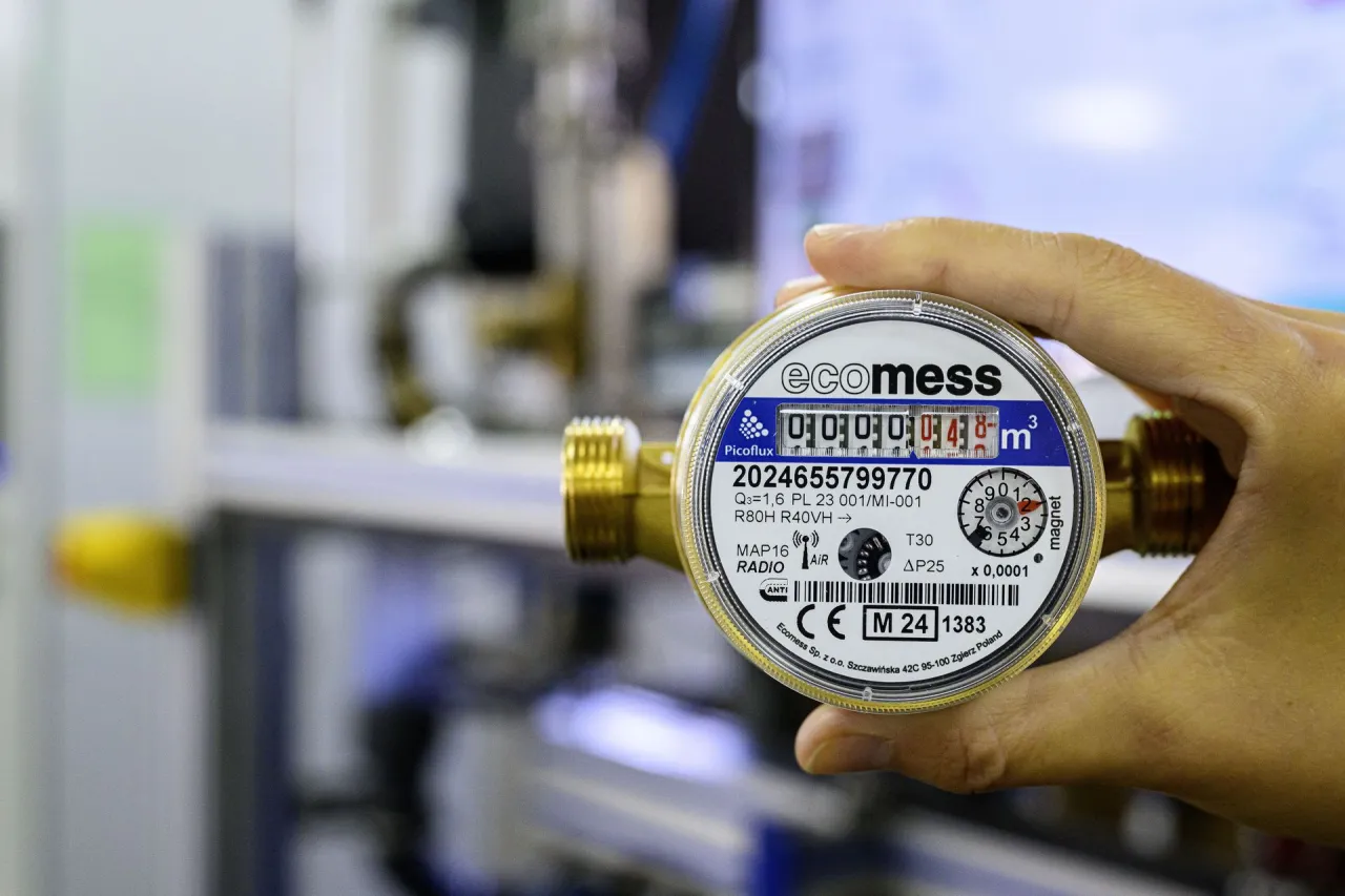 Dłoń trzyma wodomierz radiowy ecomess. Zbliżenie na licznik i oznaczenia, jak zatrzymać wodomierz radiowy.