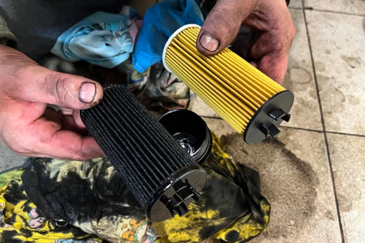Brudne ręce trzymają stary, czarny filtr powietrza i nowy, żółty. Trwa wymiana filtra powietrza.