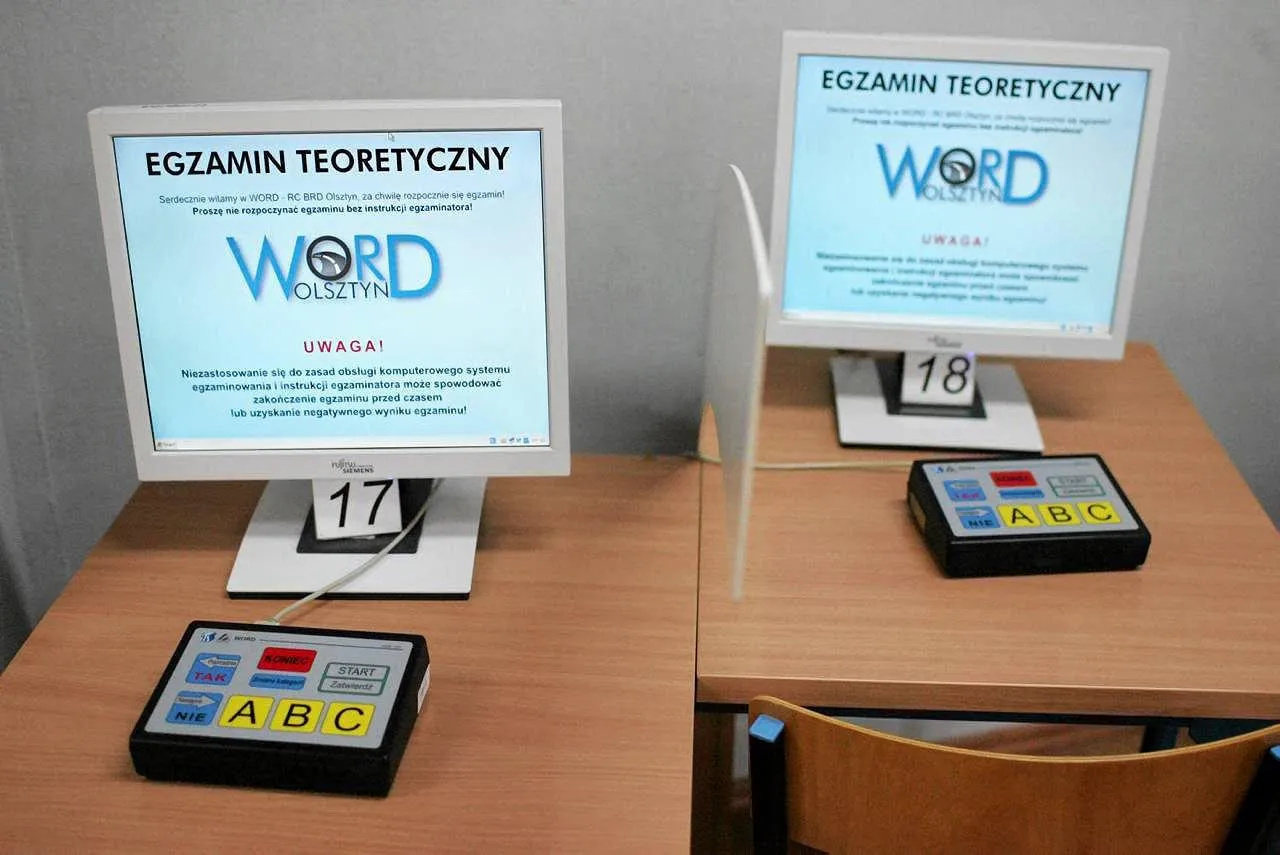 Dwa stanowiska do egzaminu teoretycznego na prawo jazdy WORD. Na monitorach informacja o egzaminie, pod nimi numery stanowisk 17 i 18. Obok przyciski do odpowiedzi.