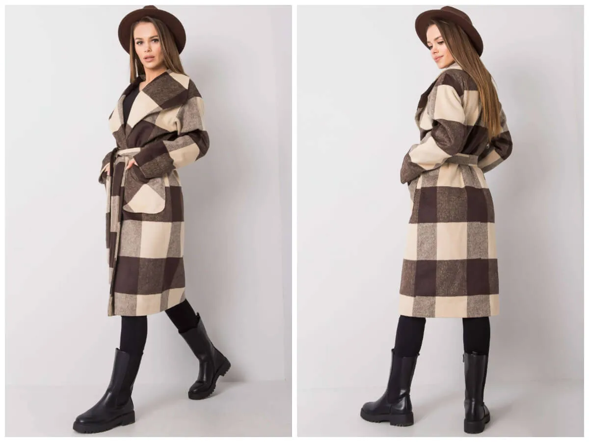 Elegancki płaszcz w kratę z paskiem, idealny na jesienne spacery. Modelka prezentuje go w stylizacji z kapeluszem i kozakami.