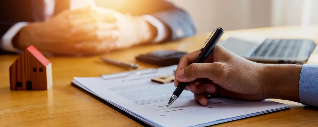 Podpisanie umowy przedwstępnej kupna mieszkania. Na stole leży model domu, długopis i dokumenty.