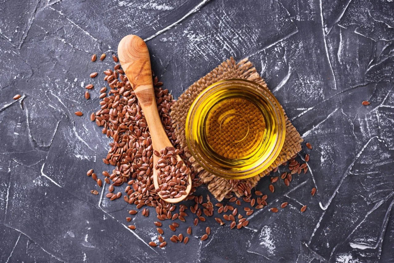 Nasiona lnu i złoty olej lniany na ciemnym tle. Czy olej lniany obniża cholesterol? Warto sprawdzić!