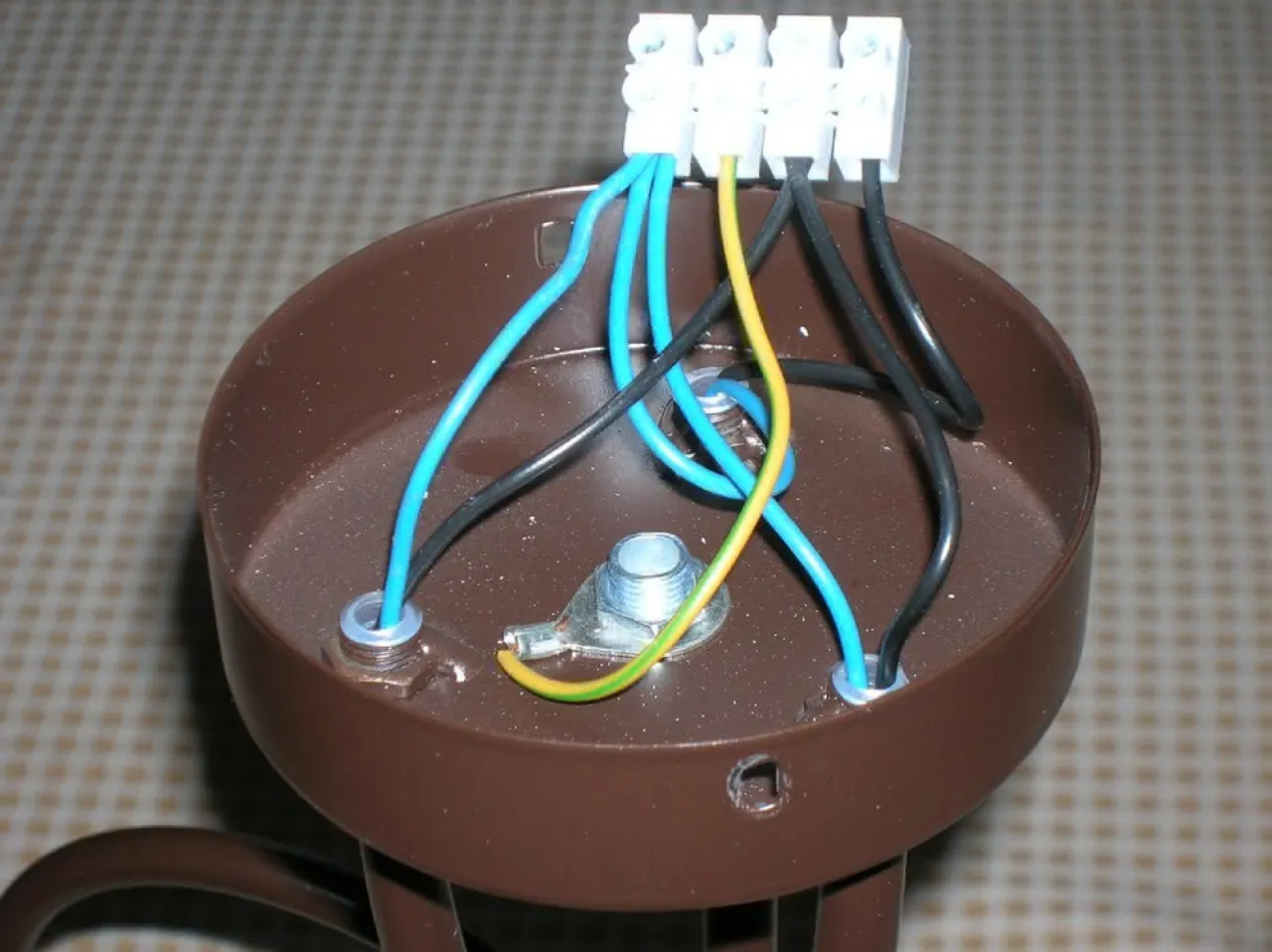 Podłączanie żyrandola LED: przewody niebieski, żółto-zielony i czarny wchodzą do brązowej obudowy przez otwory.