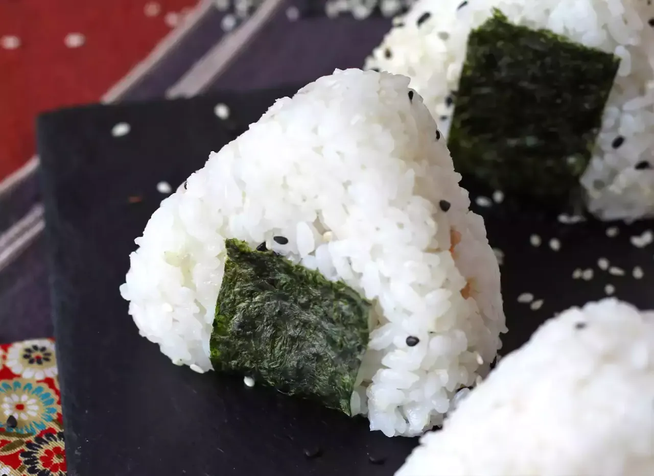 Tr&oacute;jkątne onigiri z tuńczykiem, ozdobione wodorostami nori i sezamem, wyglądają apetycznie.